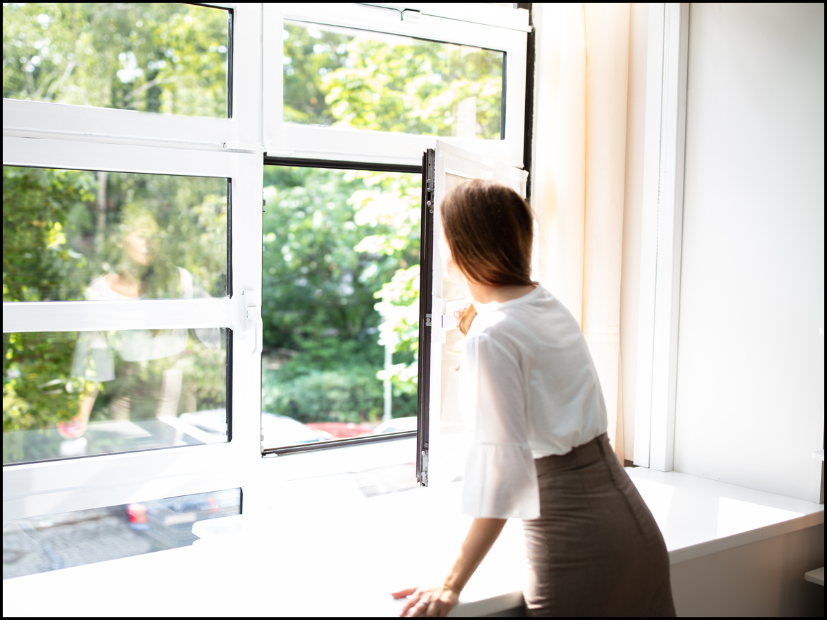 Female presenting person looking out an open window