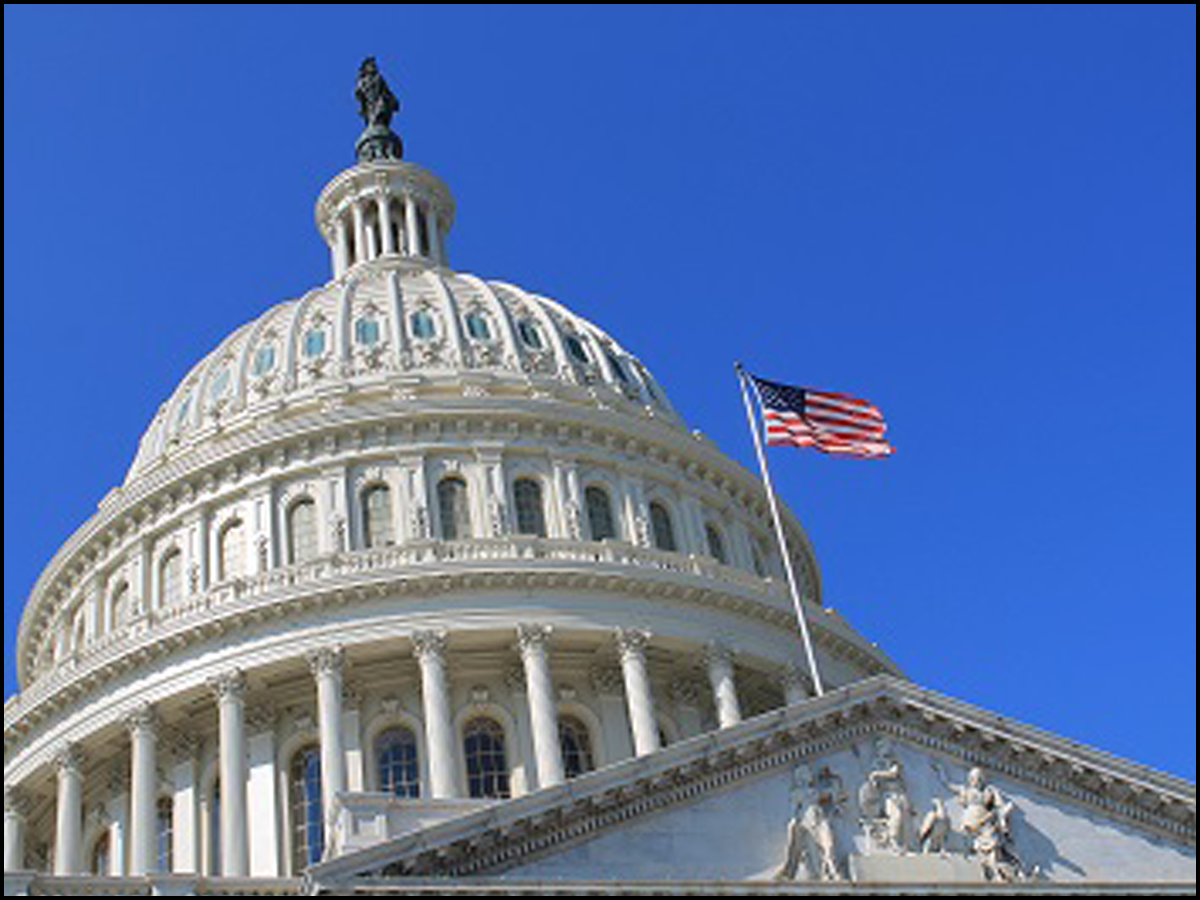 The peak of the Washington DC Capitol building with an American Flag in the wind