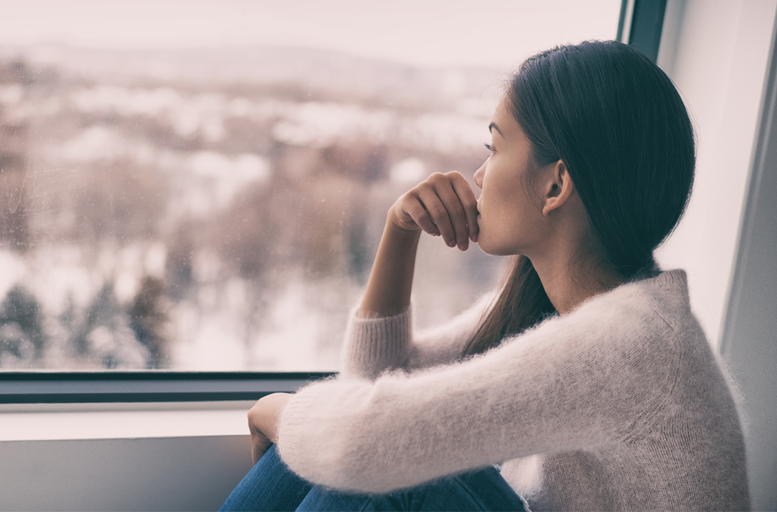 asian woman staring out a window with a wintery background