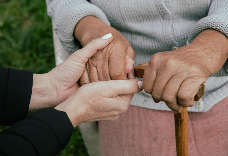 close up of caregiver holding hands of a senior woman with a cane