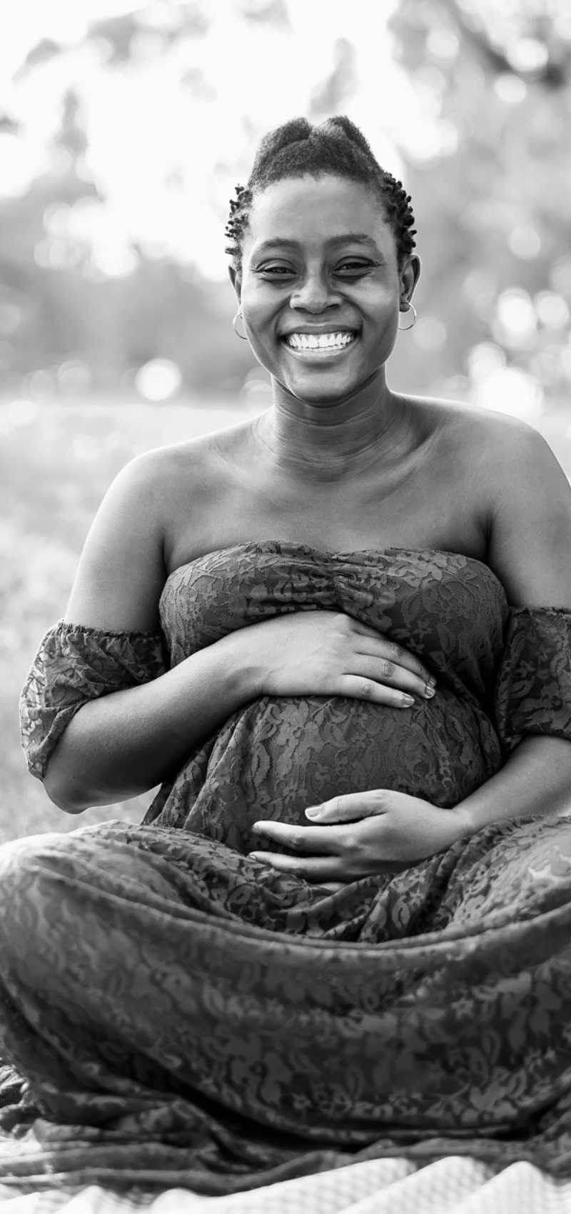 Smiling woman holding pregnant belly while sitting cross legged